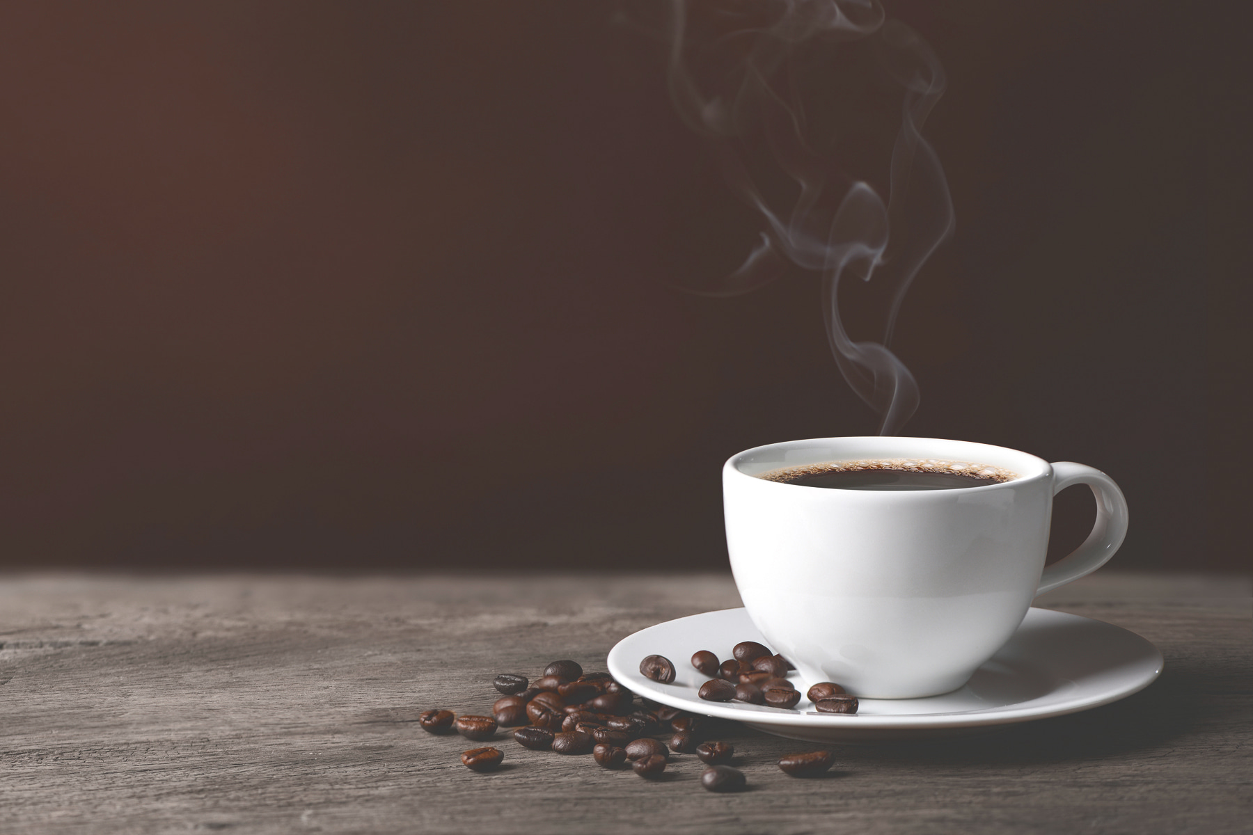 A cup of coffee with smoke and beans on a wooden surface