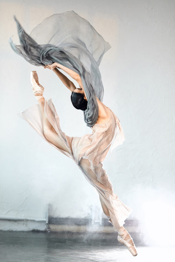 A woman in a dress and pointe shoes jumping in the air