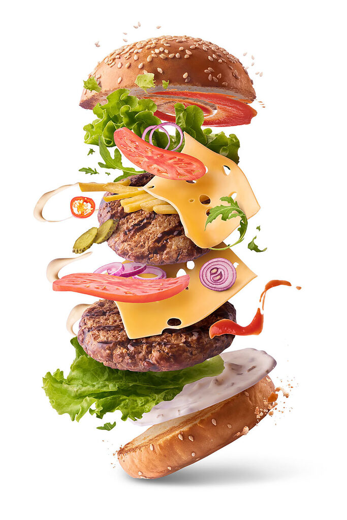 A hamburger with meat and vegetables flying in the air