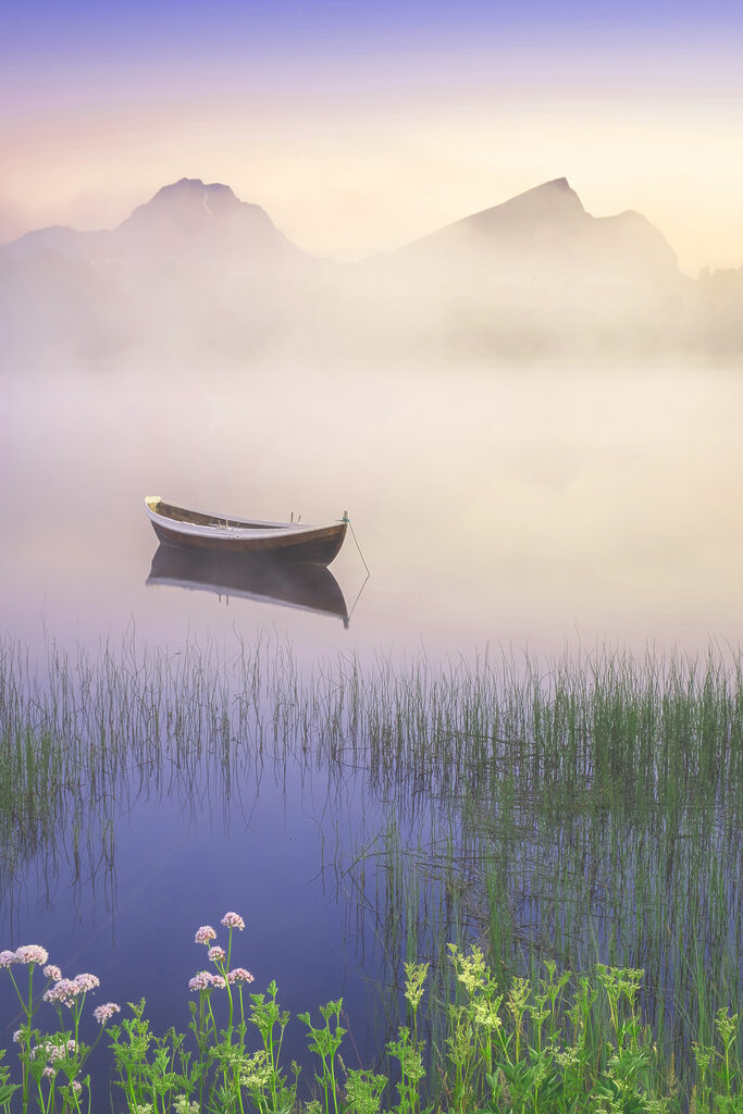 A boat in a lake with grass and mountains in the background A boat in a lake with grass and mountains in the background